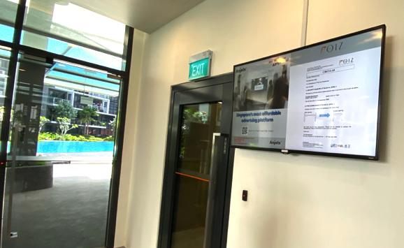 Digital advertising screen beside a condominium lobby door, with the swimming pool visible outside